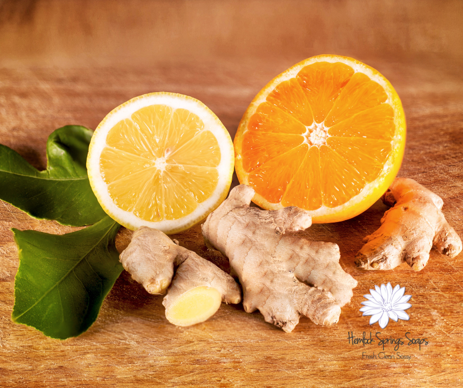 "Fresh ginger root and sliced orange and lemon on a wooden surface with green leaves, representing the bright, citrusy scent of Hemlock Springs Soaps’ Ginger Orange soap."